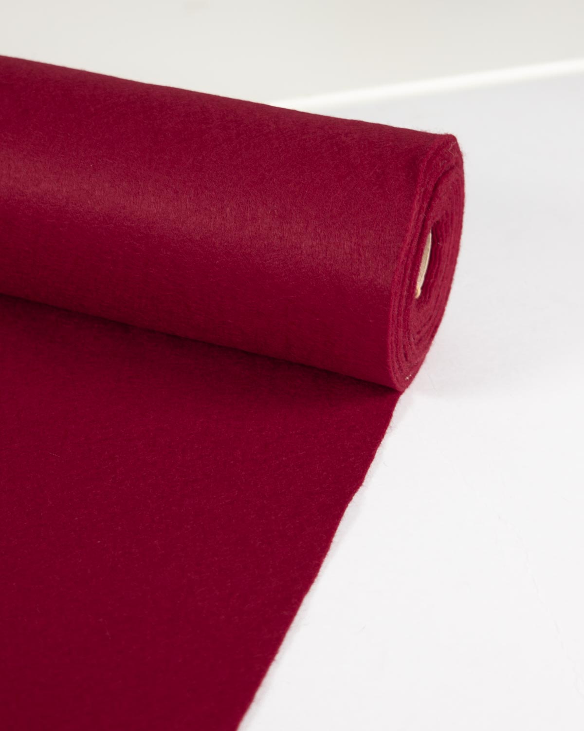 A roll of cherry red wool and viscose felt fabric partially unrolled onto a plain white surface.