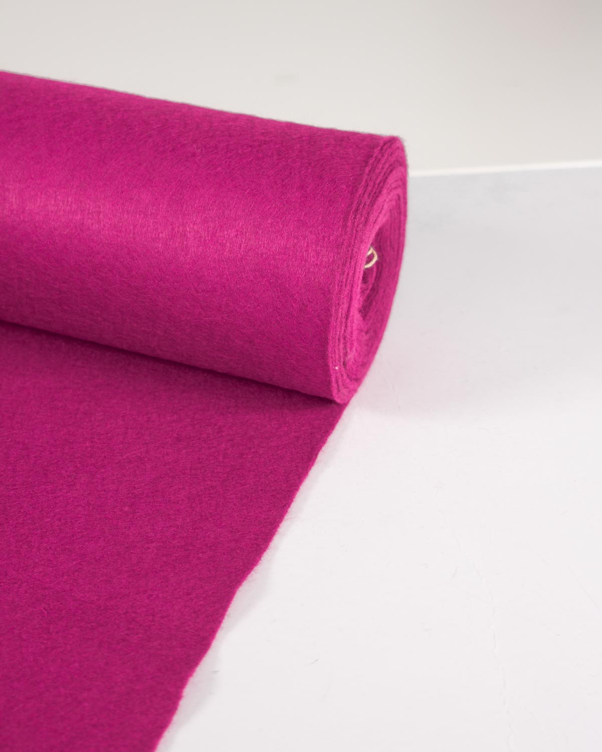 A roll of cerise pink wool and viscose felt fabric, partially unrolled onto a plain white background.