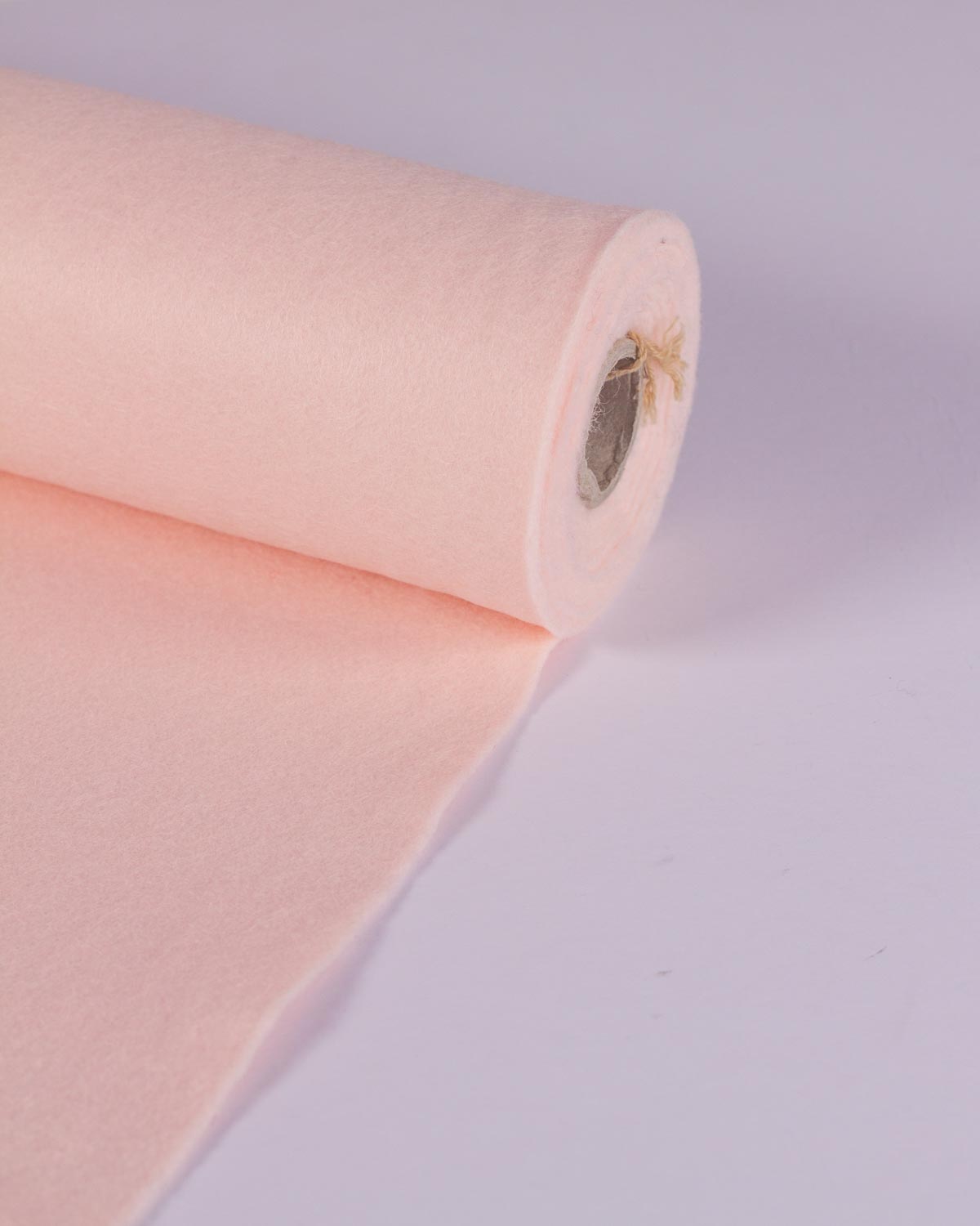 A roll of flesh pink wool and viscose felt fabric, partially unrolled onto a white surface, showing its even colour.