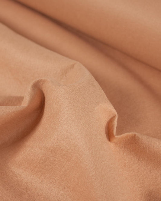 A close-up of draped peach-beige colored wool and viscose felt fabric with soft folds and a smooth texture.