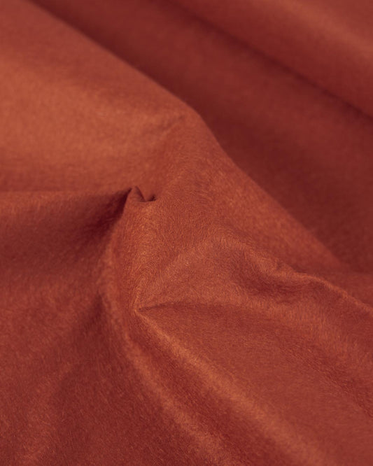 A close-up of draped terracotta colored wool and viscose felt fabric with a soft, slightly fuzzy texture.