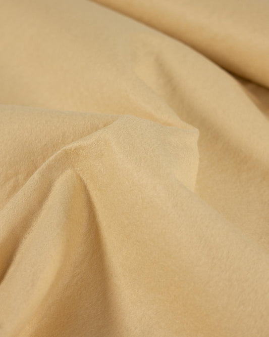A close-up of draped biscuit-cream wool and viscose felt fabric with soft folds and a smooth, matte texture.