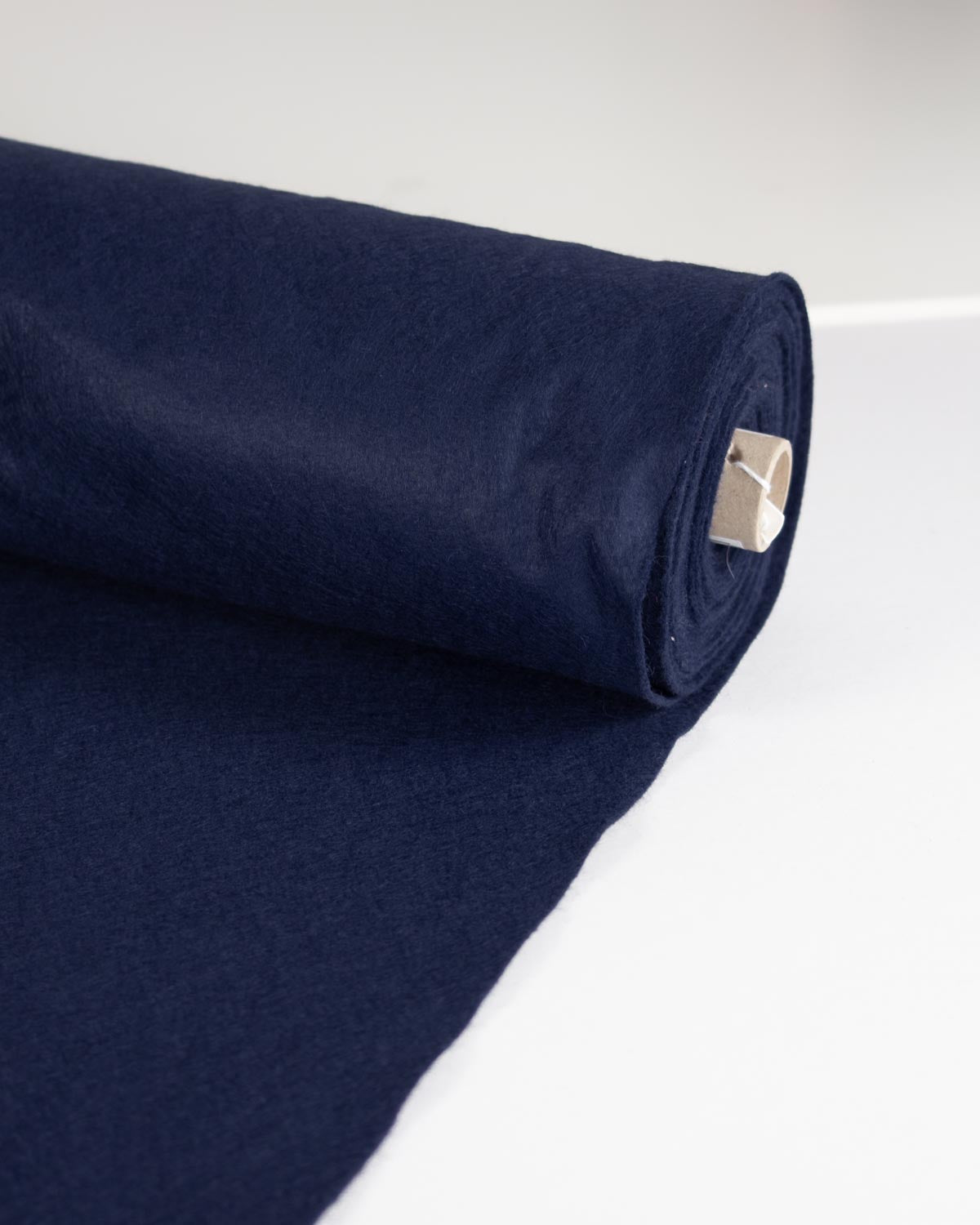 A roll of dark navy blue wool and viscose felt fabric with a matching flat sheet unrolled on a clean white background.