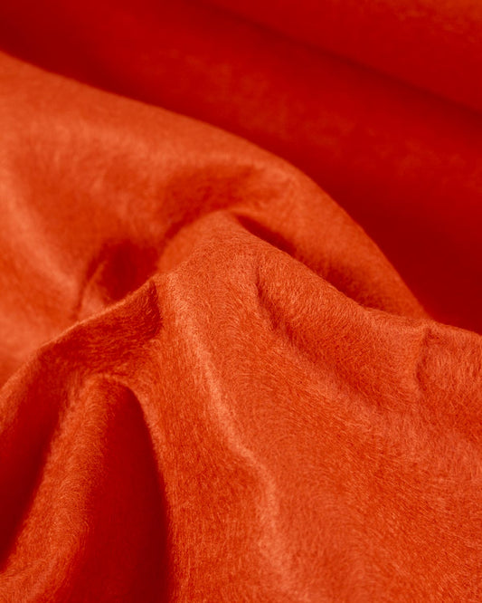 A close-up of draped bright orange wool and viscose felt fabric with soft folds and a smooth, slightly lustrous texture.