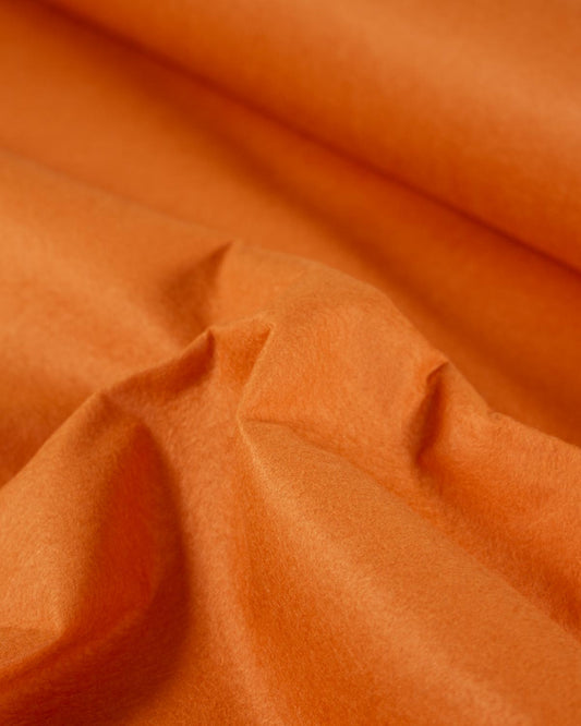 A close-up of draped light orange fabric with soft folds and a smooth, slightly matte texture.