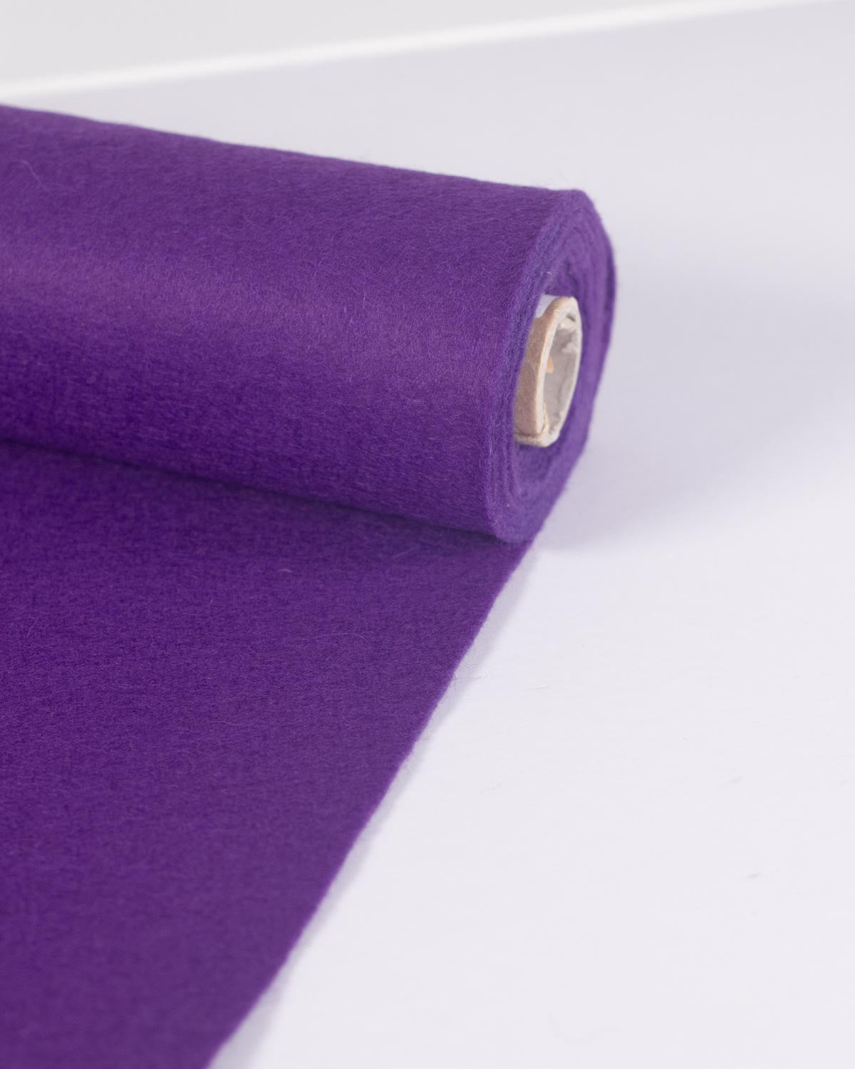 A roll of purple wool and viscose felt fabric, partially unrolled onto a plain white surface, showing its even and bold colour.