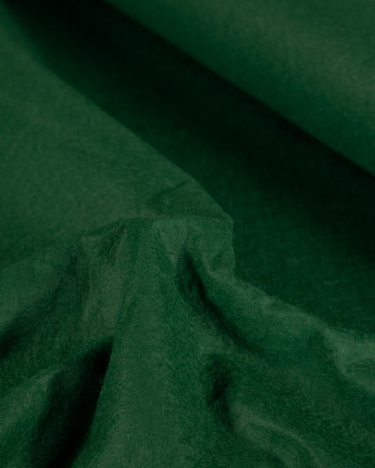 A close-up of dark forest green textured wool and viscose felt fabric with soft folds and a rolled corner, filling the entire frame.