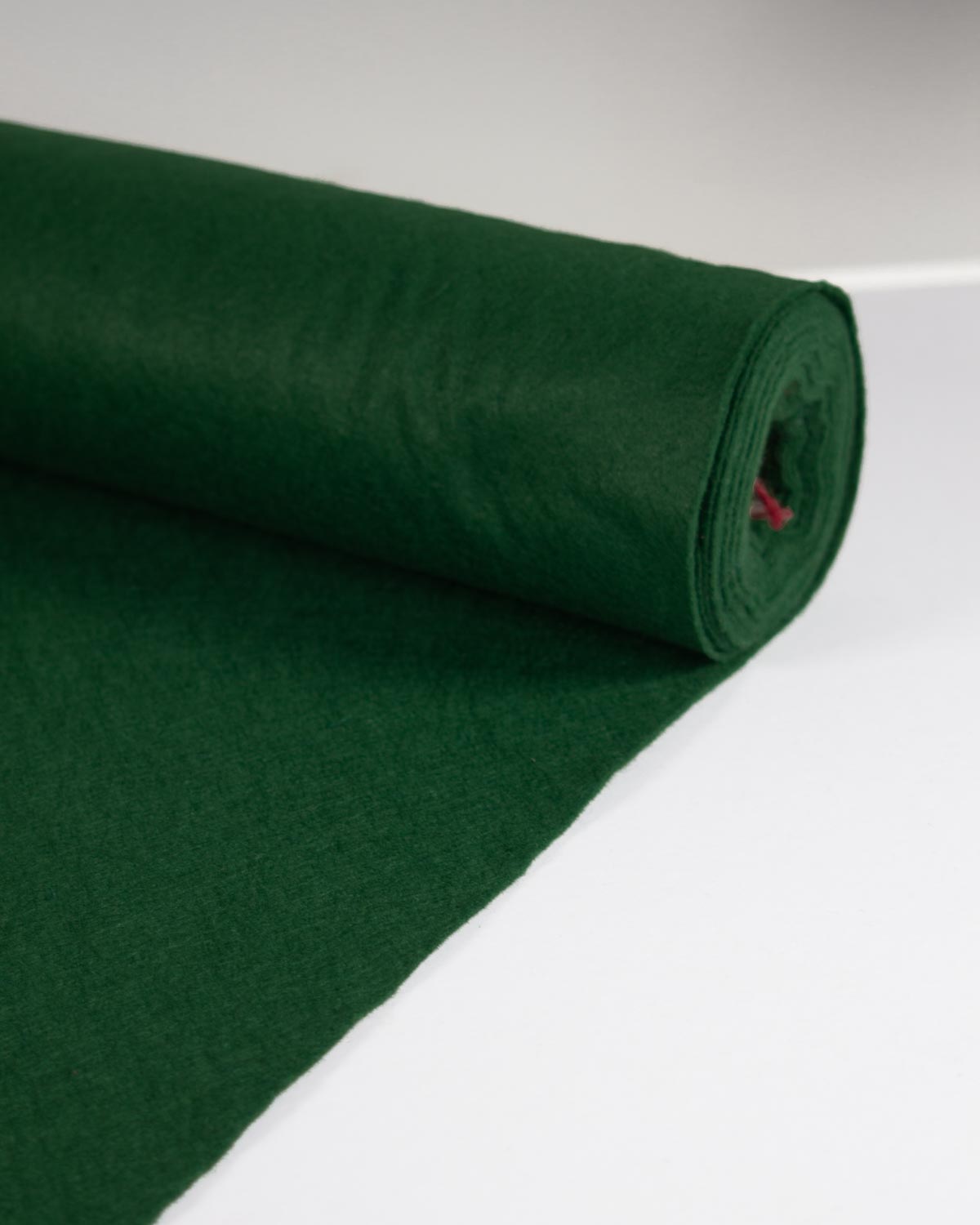A roll of holly green wool and viscose felt fabric partially rolled out on a flat white surface.