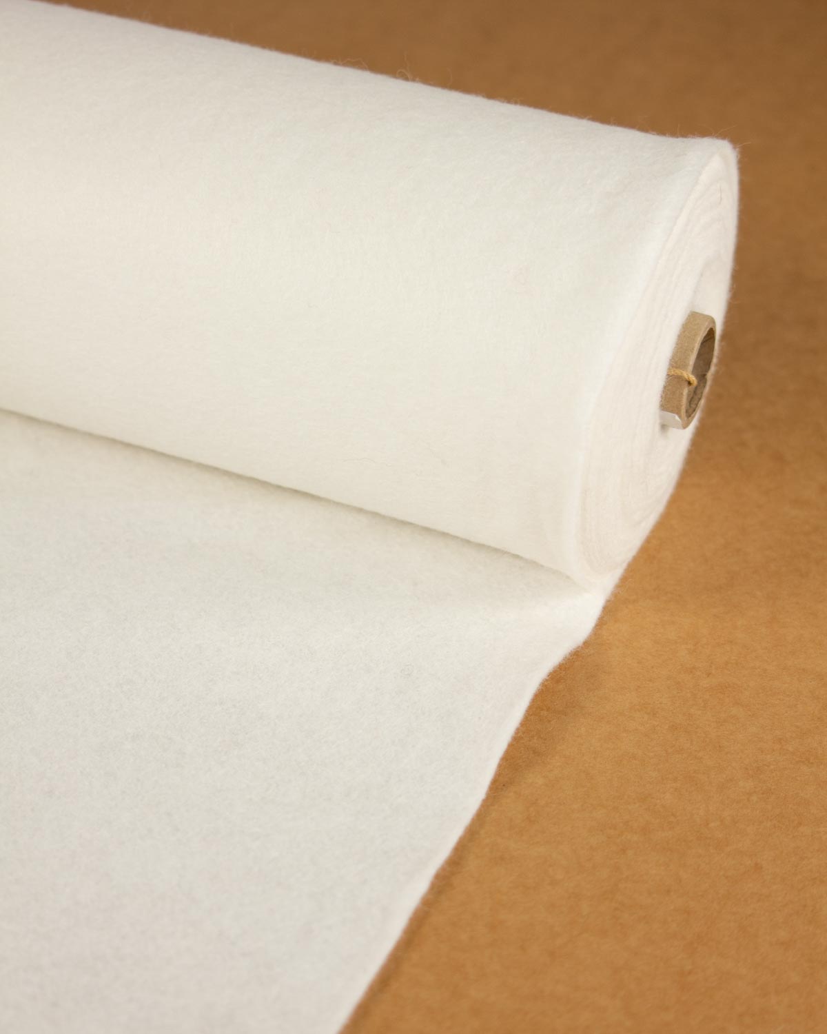 A roll of natural off-white wool and viscose felt fabric partially unrolled onto a brown surface.
