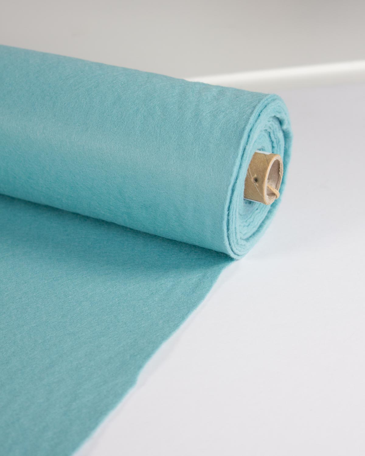 A roll of light turquoise blue wool and viscose felt fabric unrolled on a clean white surface.