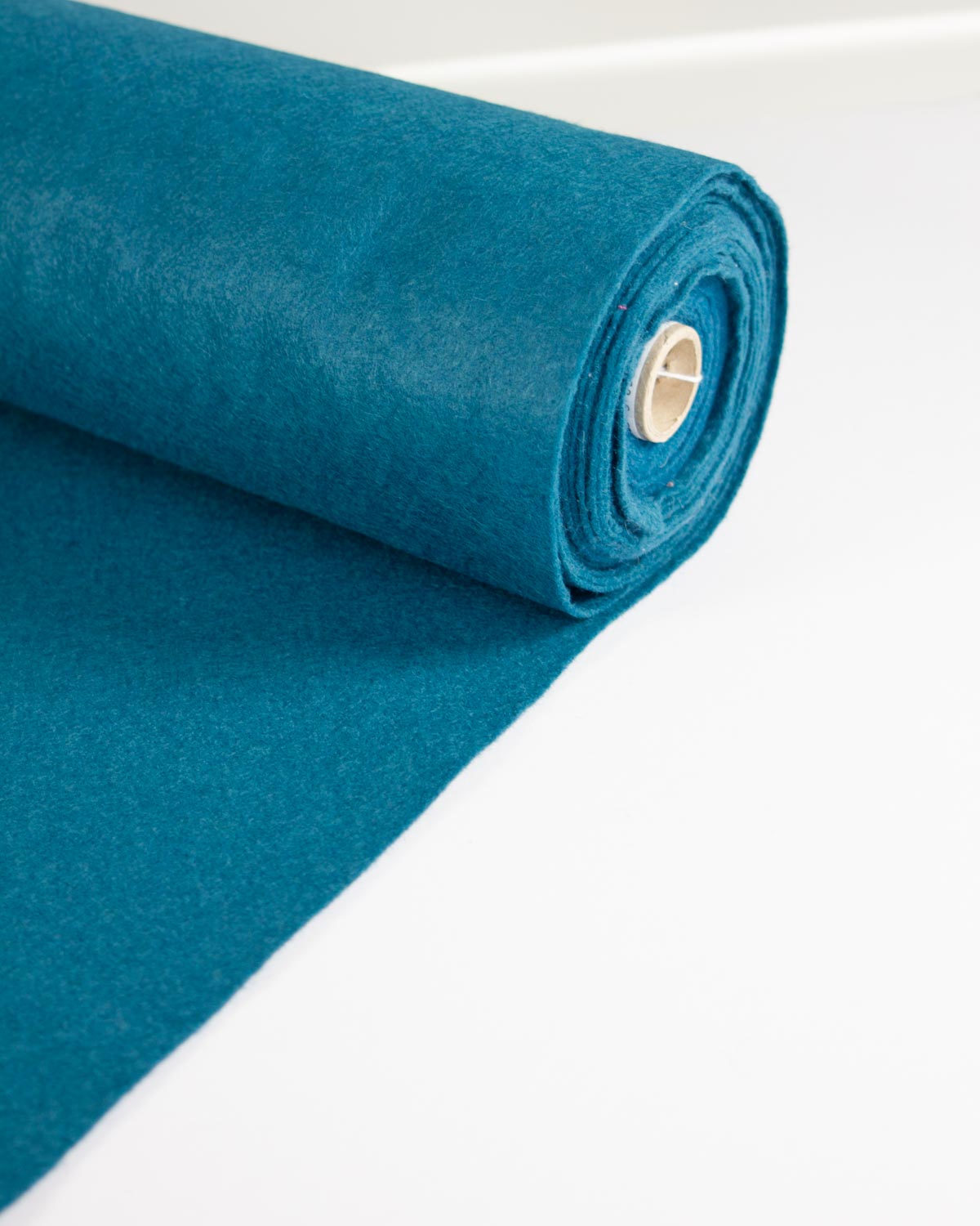 A roll of teal blue wool and viscose felt fabric, partially unrolled, shown on a clean white background.