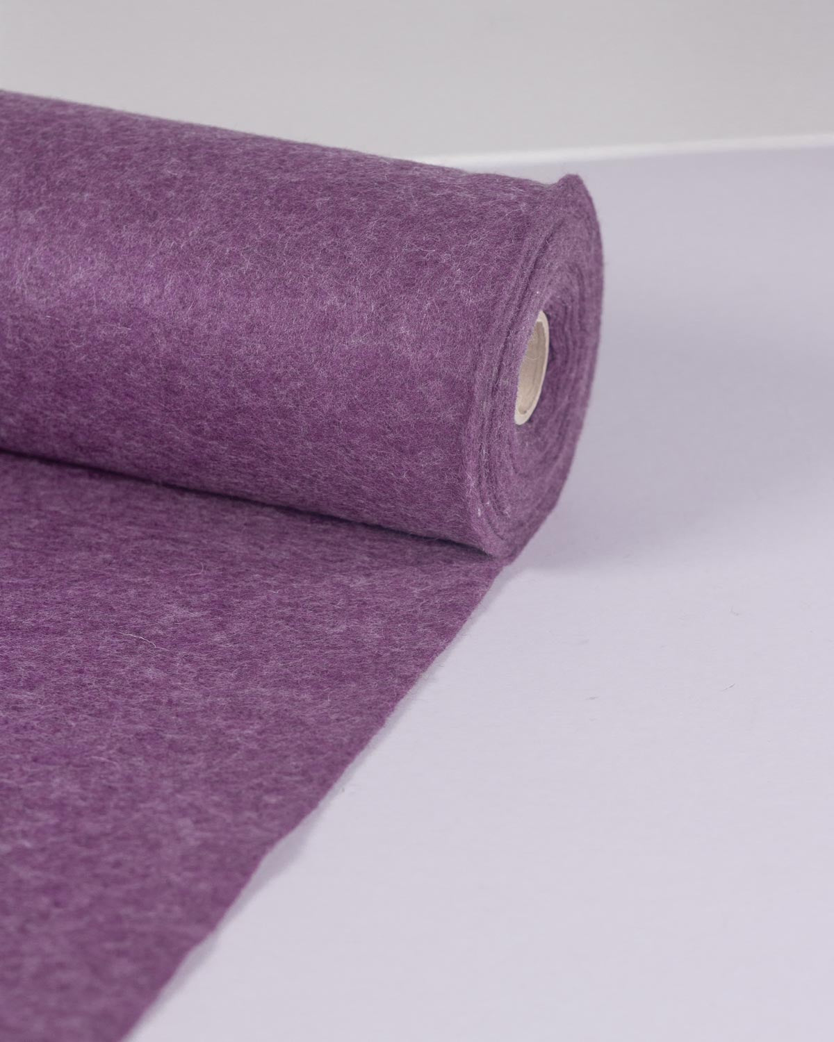 A roll of wool and viscose felt fabric, partially unrolled onto a white backdrop.