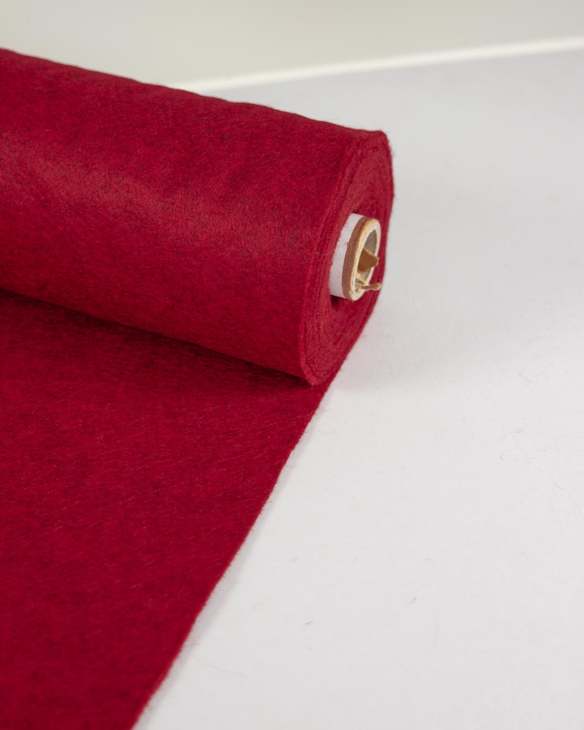 A roll of red marl wool and viscose felt fabric partially unrolled onto a white background.