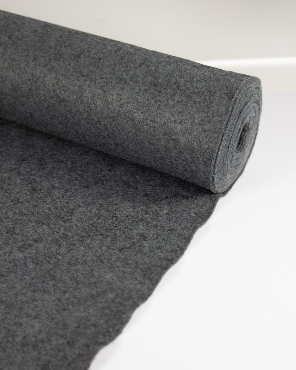 A roll of soot marl wool and viscose felt fabric rolled out onto a flat white surface.