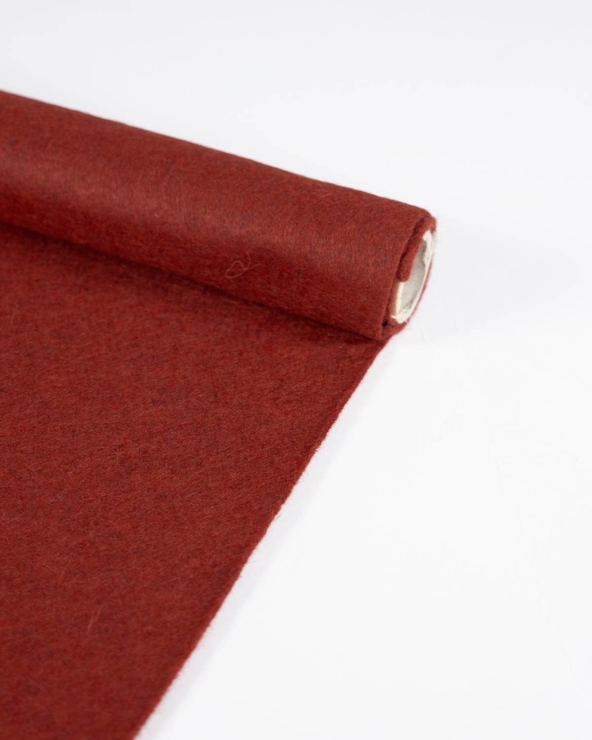 A roll of terracotta red/orange wool and viscose felt fabric partially unrolled onto a plain white surface.