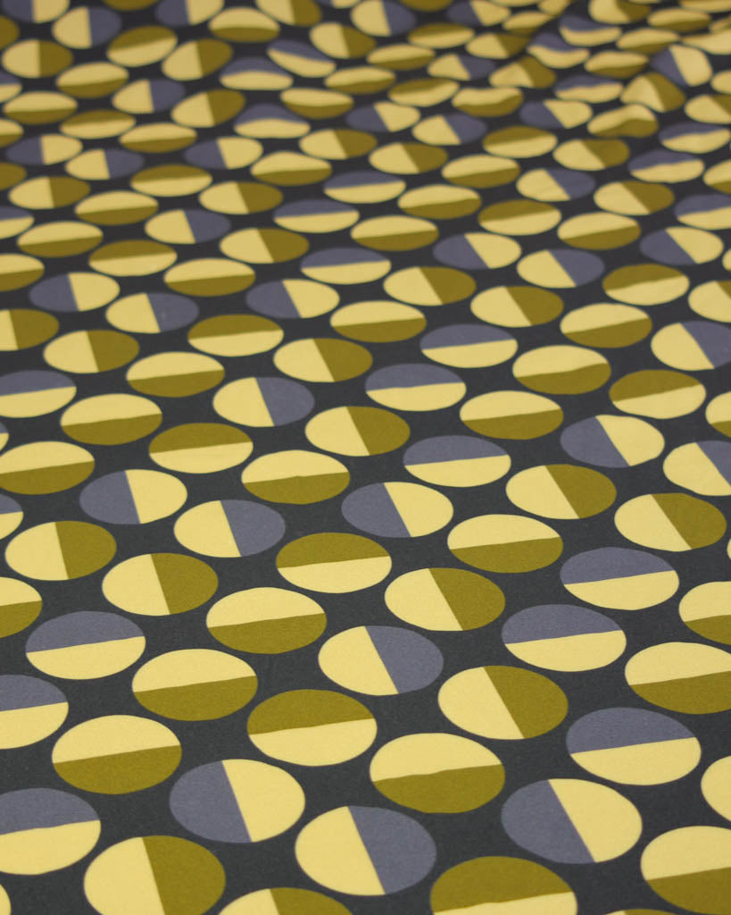 Patterned viscose twill fabric with green and yellow circle shapes on a dark background