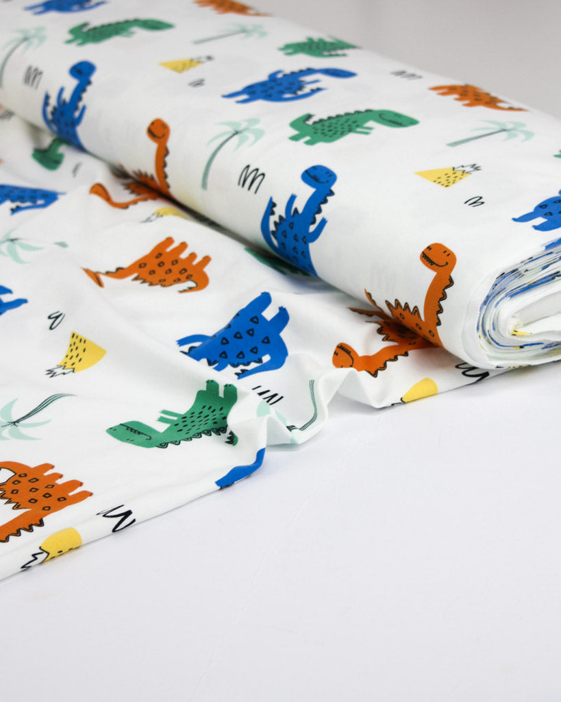 Roll of cotton jersey fabric with colorful dinosaur pattern on a white background