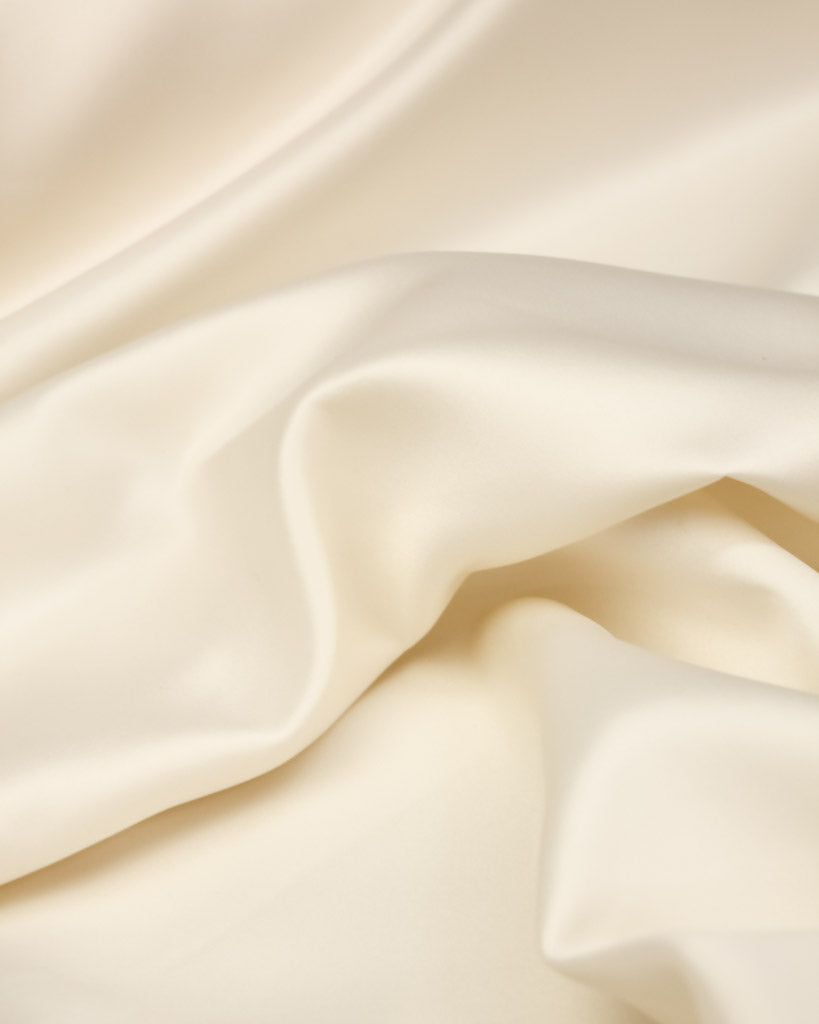 Close-up of smooth, cream satin fabric with soft folds