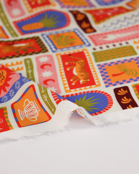 Colourful viscose fabric with patterned holiday stamp design on a white background featuring illustrations of tigers, seashells, suns, palm trees, fruit, pineapples, bananas and tropical imagery