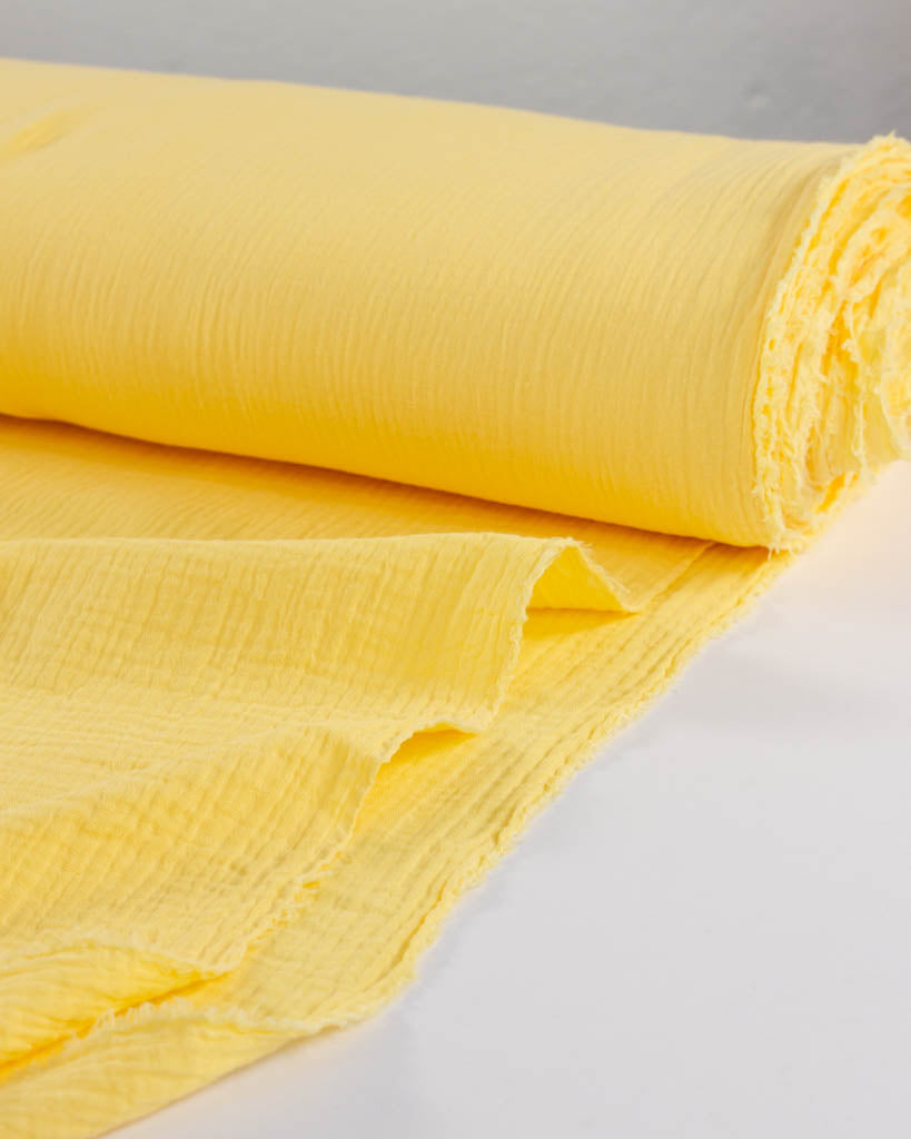 Roll of banana yellow double cotton gauze fabric on a white surface