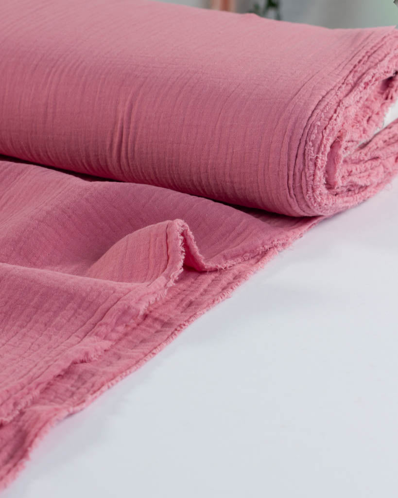 Pink textured cotton double gauze fabric rolled up on a white surface