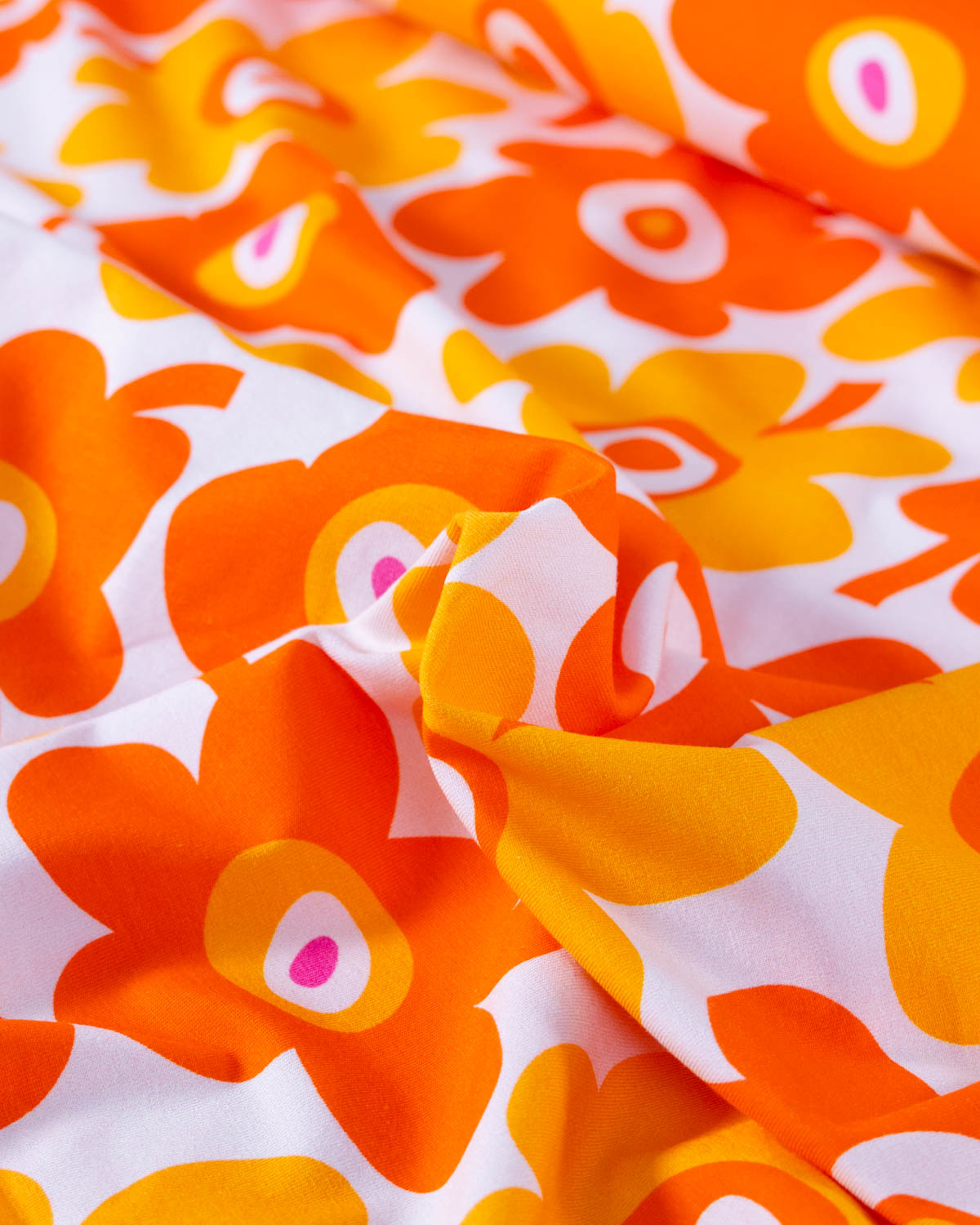 Close-up of orange floral pattern on white cotton jersey fabric