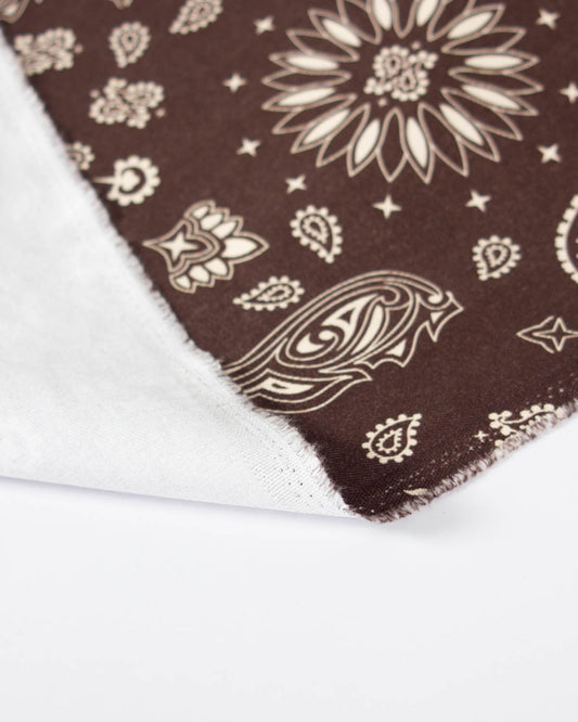 A close-up of a brown bandana print denim fabric with a cream paisley and floral print.