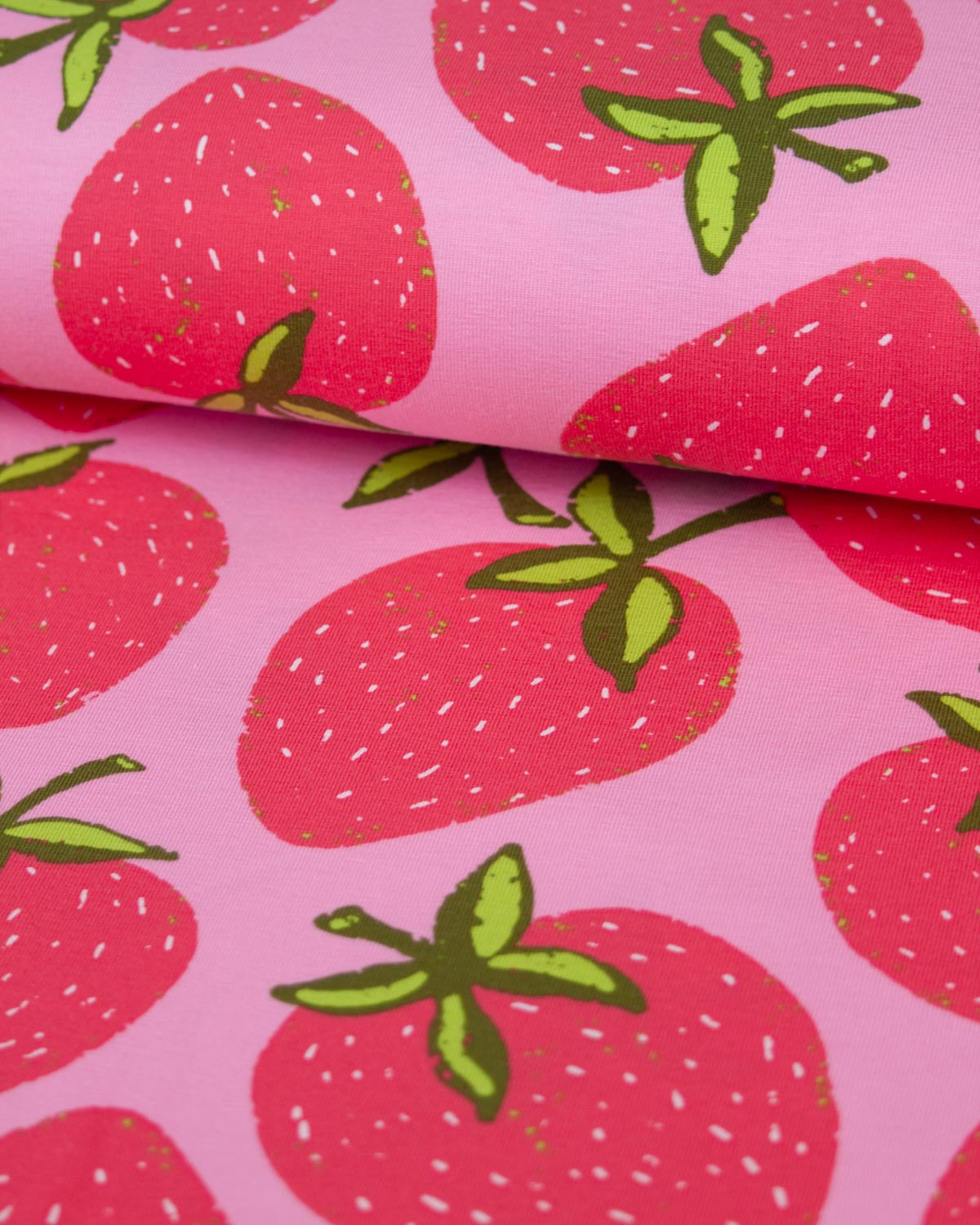 Pink cotton jersey fabric with a repeating strawberry print, featuring red strawberries with green leaves and small white speckles.