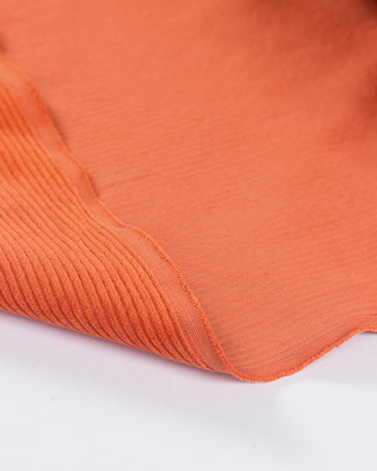 A close-up of a folded orange cotton corduroy fabric with a fine ribbed texture, showing its colour and material detail against a white background.