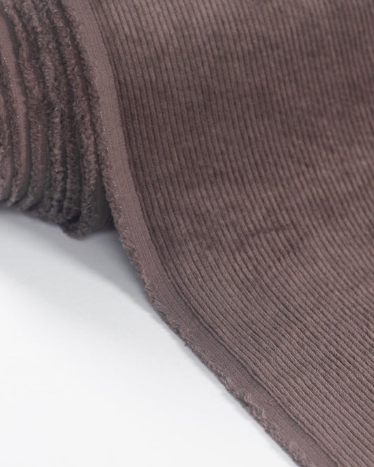 A close-up of a ribbed cotton corduroy fabric in a muted taupe-brown color, folded over to show its texture against a plain white background.