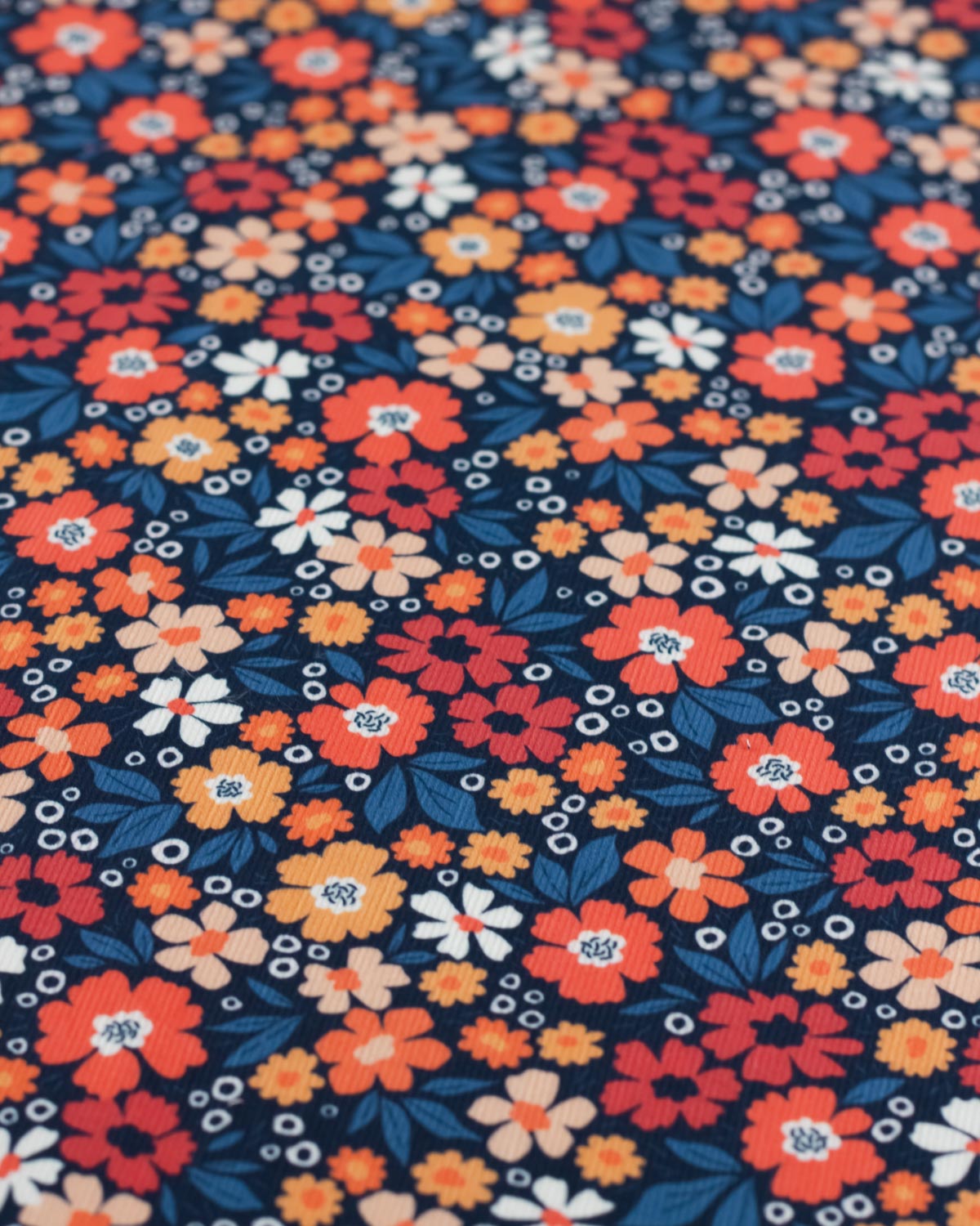 A close-up of a navy blue cotton babycord fabric with a dense, colorful floral pattern featuring orange, red, yellow, and white flowers with blue leaves.