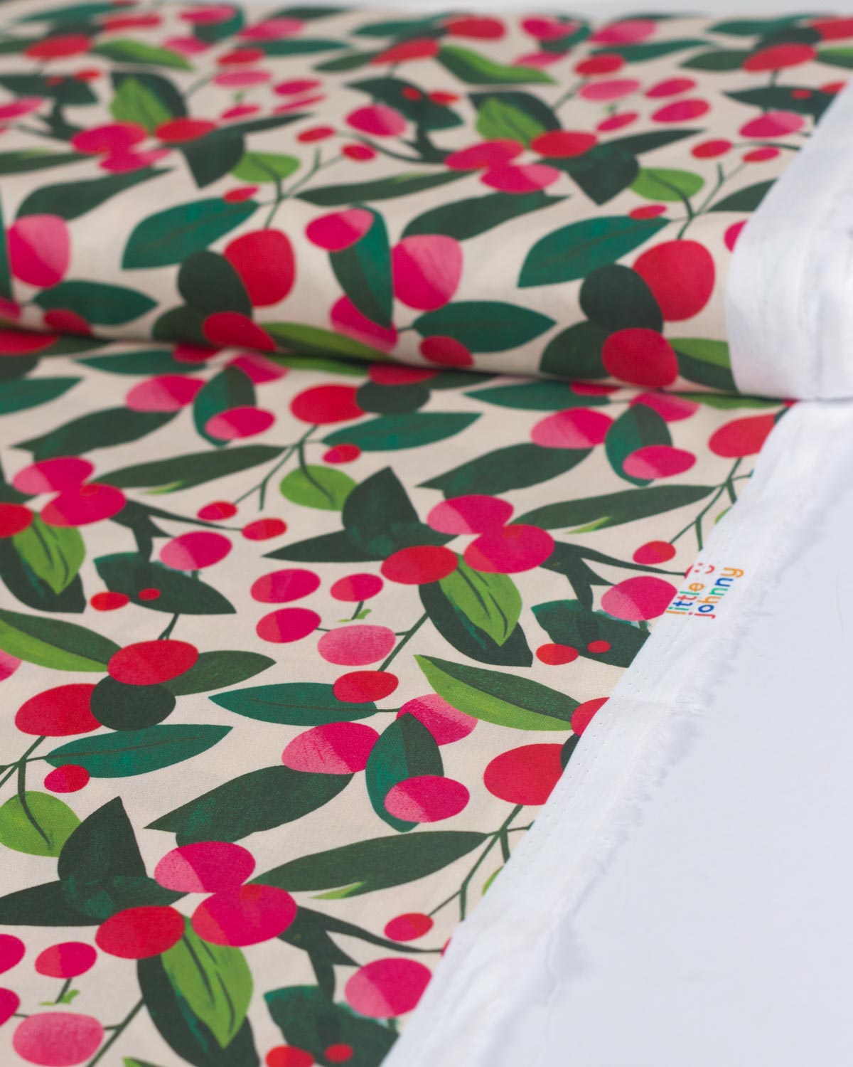 A close-up of a printed christmas cotton fabric featuring a repeating pattern of red berries and green leaves on a cream background.