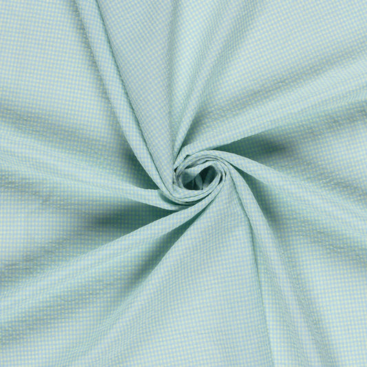 A close-up of light blue and yellow fabric with a fine micro-check pattern, artistically swirled in the center to show its drape and texture.