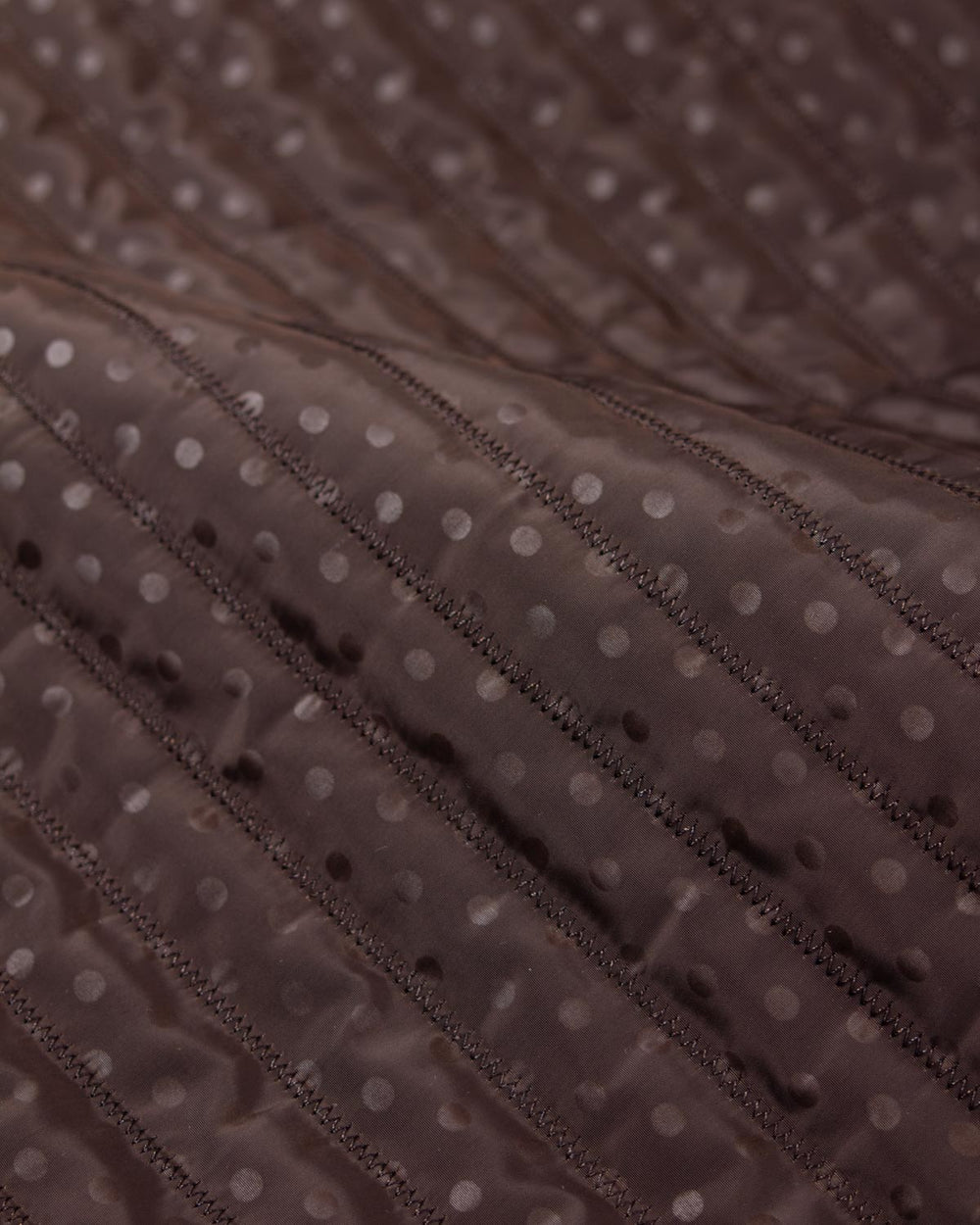 Chocolate brown showerproof quilted fabric with a white polka dot print and zigzag quilting over padded wadding.