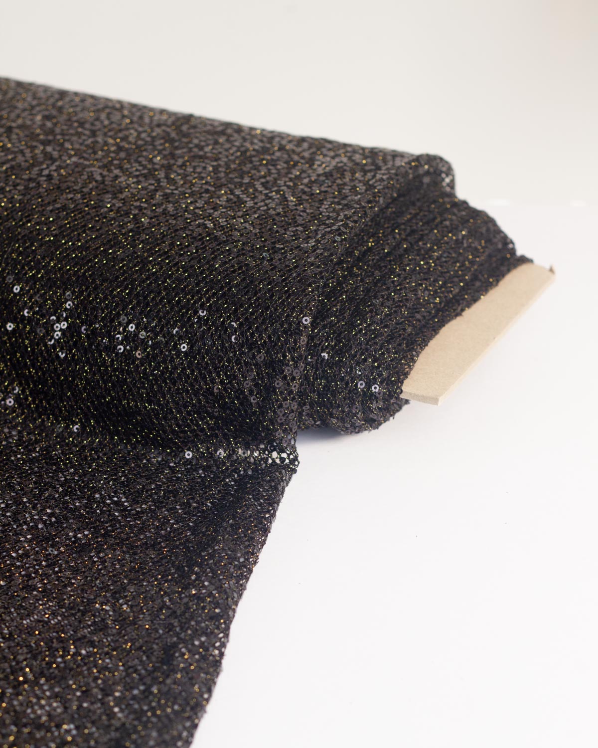 A close-up of a black tulle sequined fishnet fabric roll with a light cardboard backing, photographed on a plain white background.
