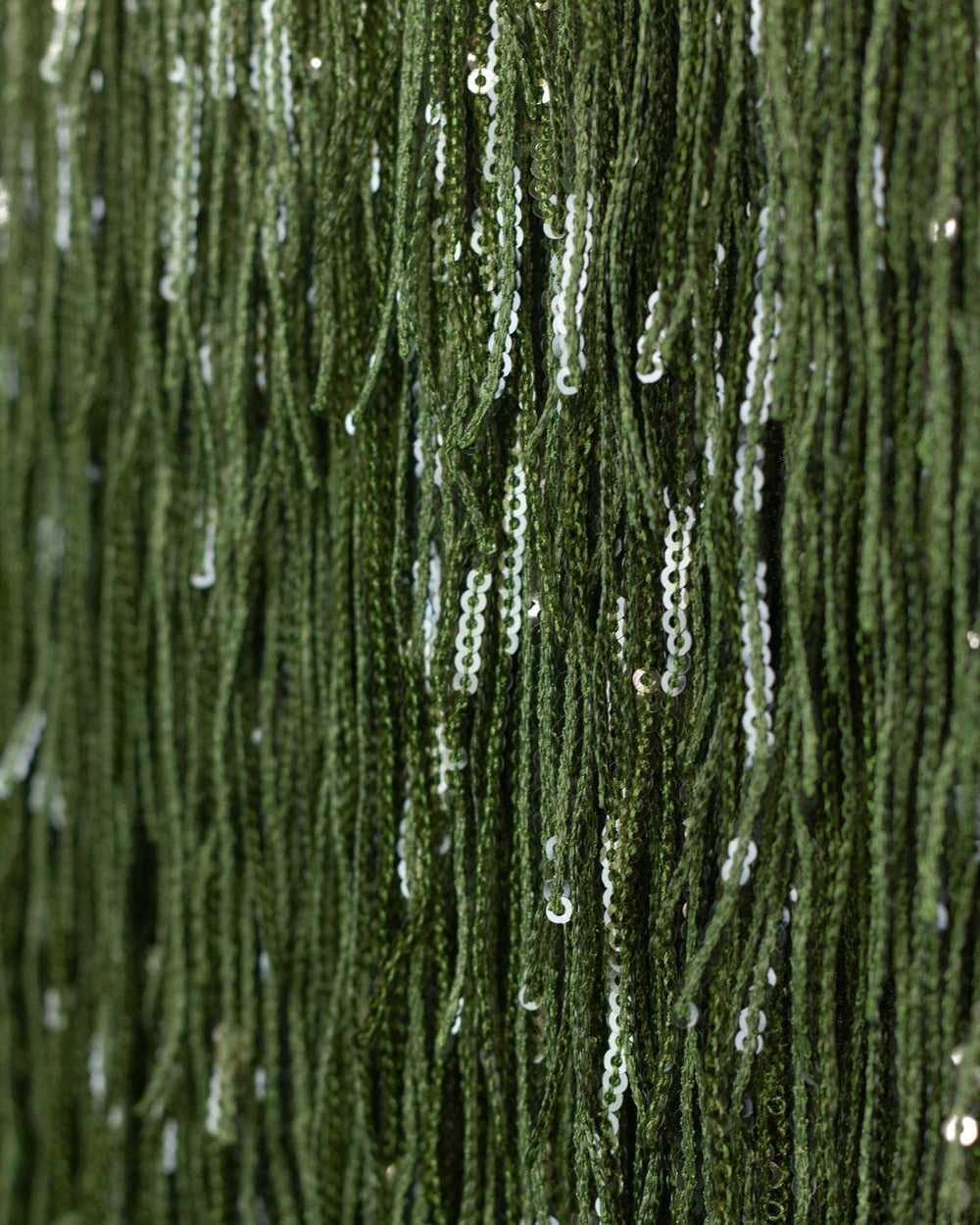Close-up of dark green fringe polyester fabric adorned with dangling silver sequins.