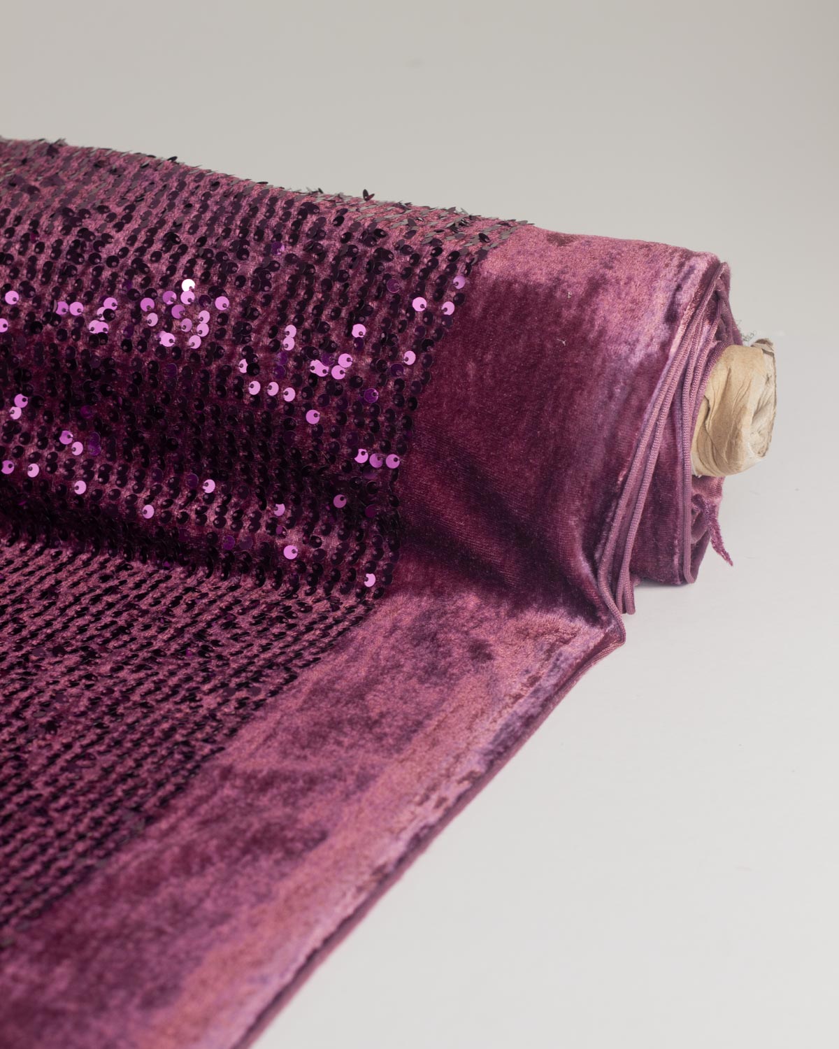A roll of deep purple velvet fabric with sequined texture, unrolled on a white background