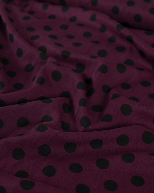 A close-up of draped viscose twill fabric in a deep burgundy or plum purple color with a repeating black polka dot pattern.