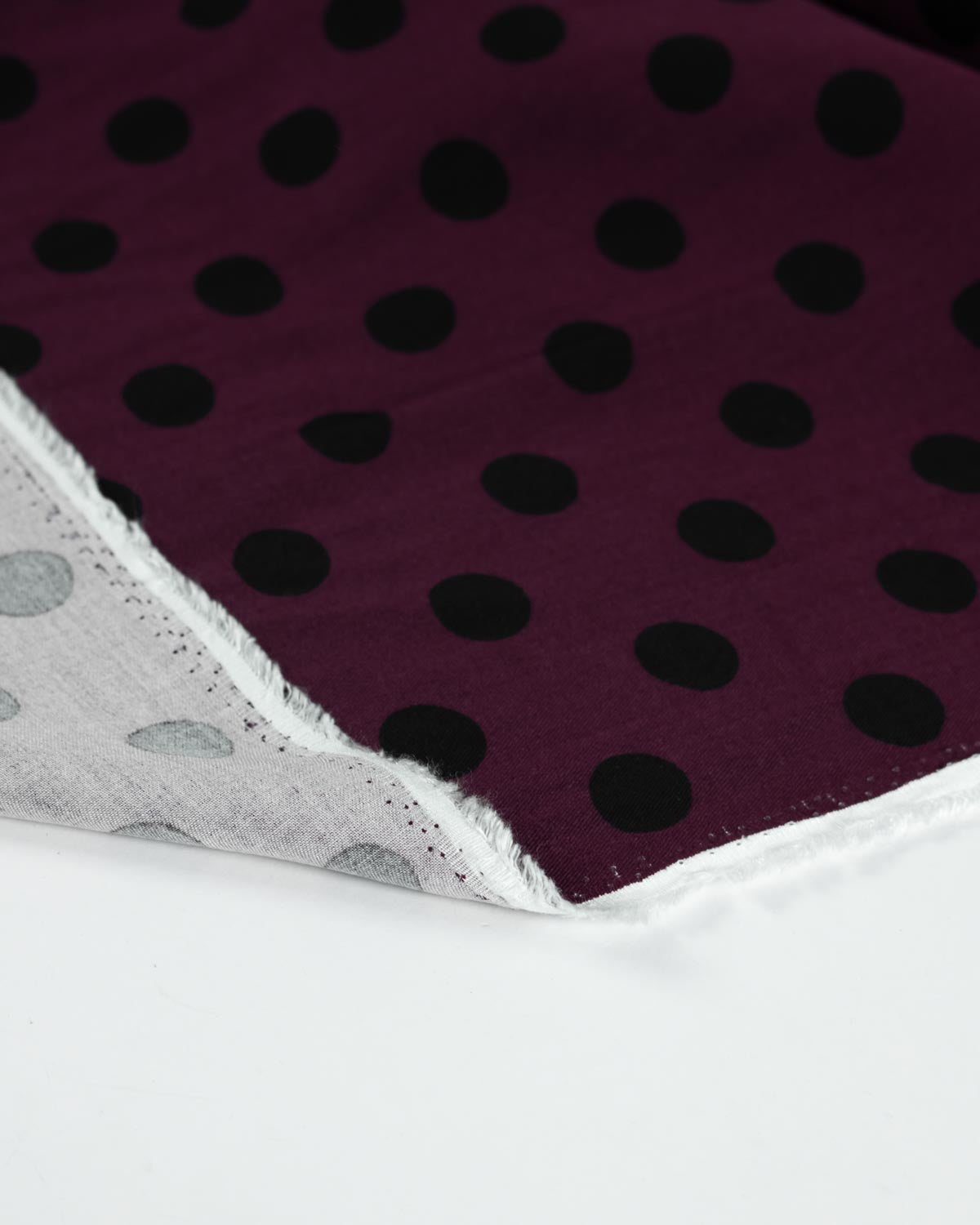 A close-up of a viscose fabric showing a deep purple front side with black polka dots.