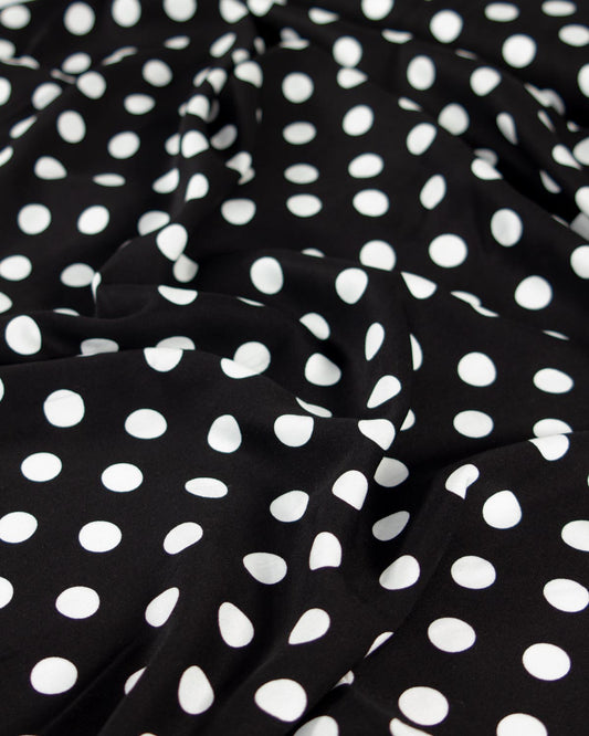 Black viscose twill fabric with a white polka dot pattern, shown with soft folds and ripples.