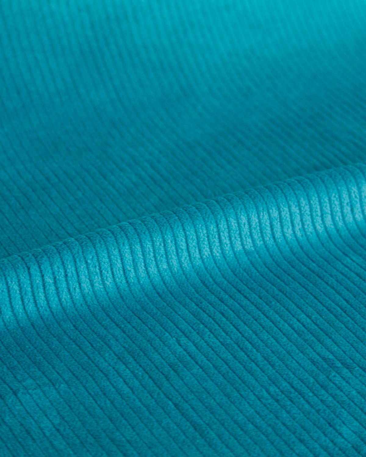 A close-up of a teal blue corduroy fabric texture, showing the vertical ridges and soft folds.