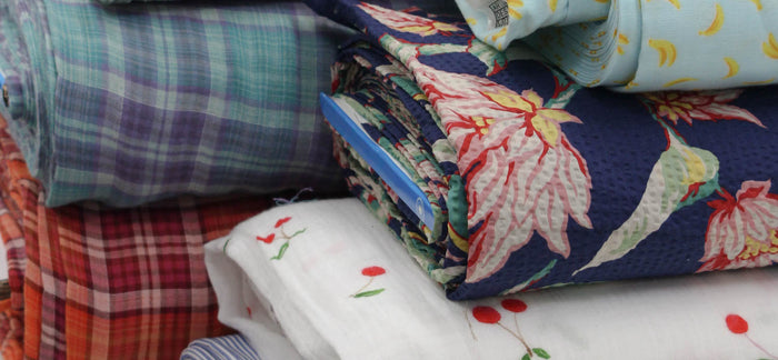 Stacked rolls of deadstock fabrics in different colours and textures, including cottons and linens.