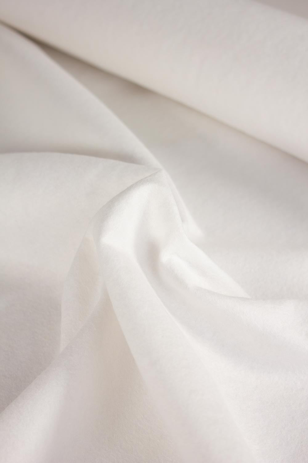 A close-up of draped white wool and viscose fabric with soft folds and a rolled section at the top, showing a smooth matte texture.