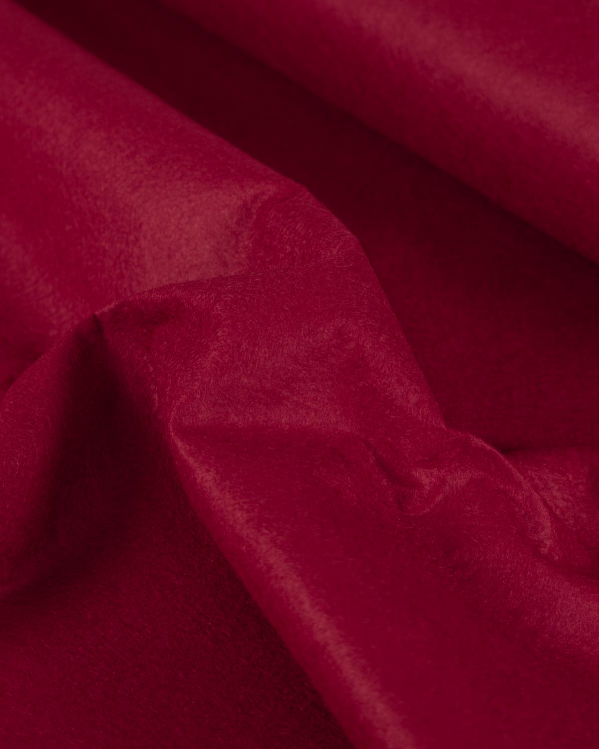A scrunched up piece of wool and viscose felt fabric in cherry red, with its deep colour and textured surface on show. 