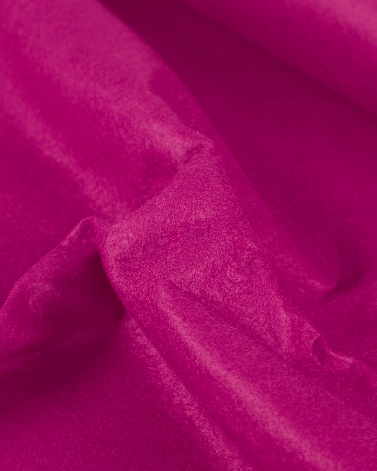A piece of cerise pink wool and viscose felt fabric gathered up to show its firm structure and texture. 
