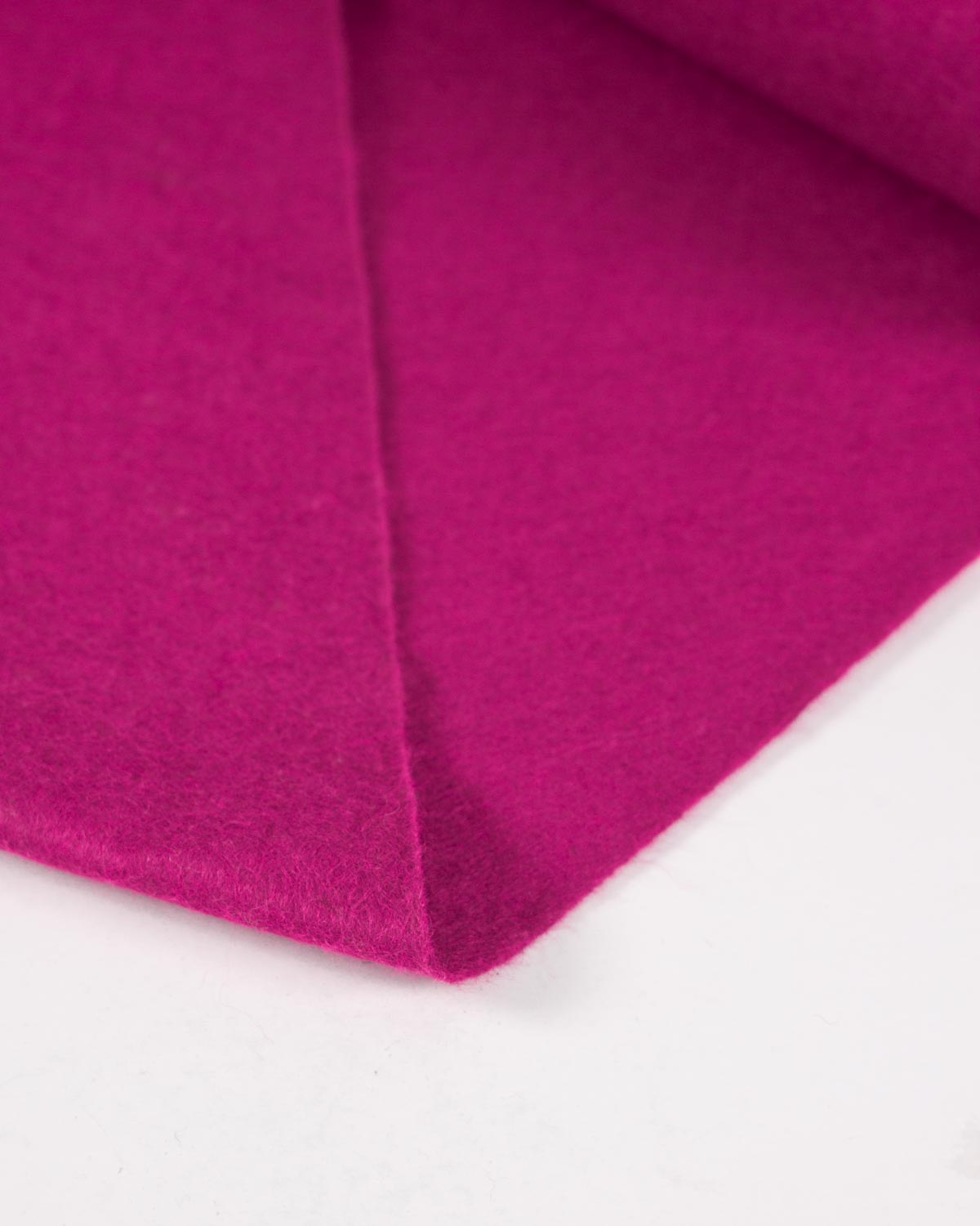 A piece of wool and viscose felt fabric in cerise pink folded on a white background, showing its bold colour and textured surface.