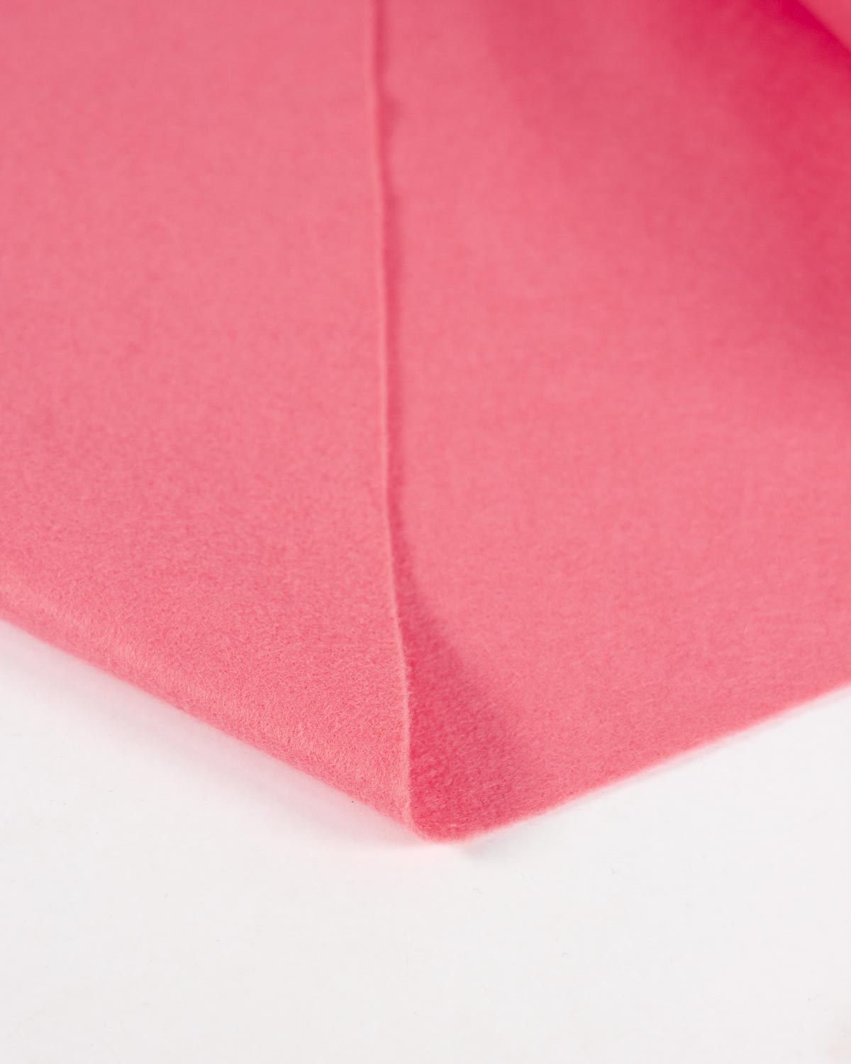 A piece of rose pink wool and viscose felt fabric, folded over on a white surface to show its bright, bold colour and texture.