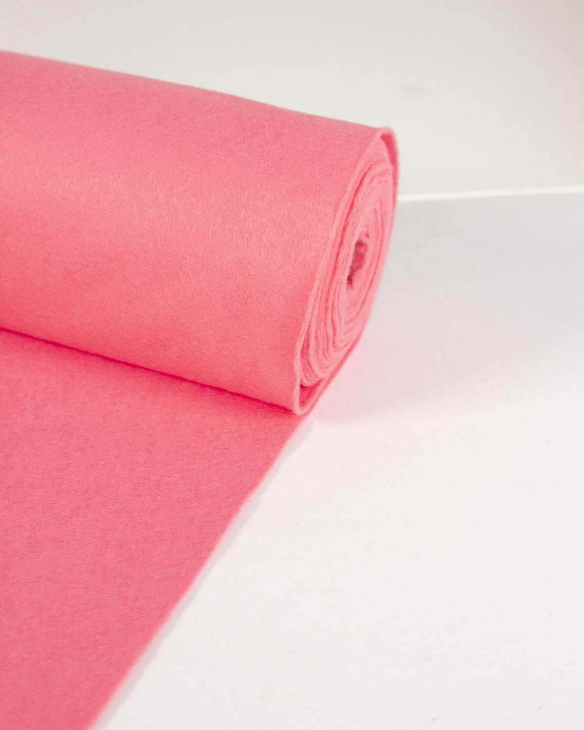 A roll of rose pink wool and viscose felt fabric, partially unrolled onto a white surface. 