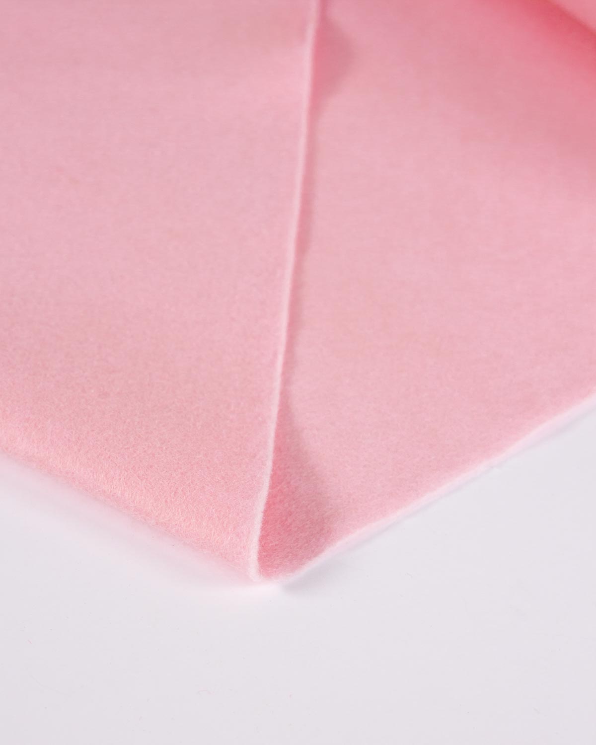 A piece of candy pink wool and viscose felt fabric, folded on a plain white surface to show its even colour and texture.