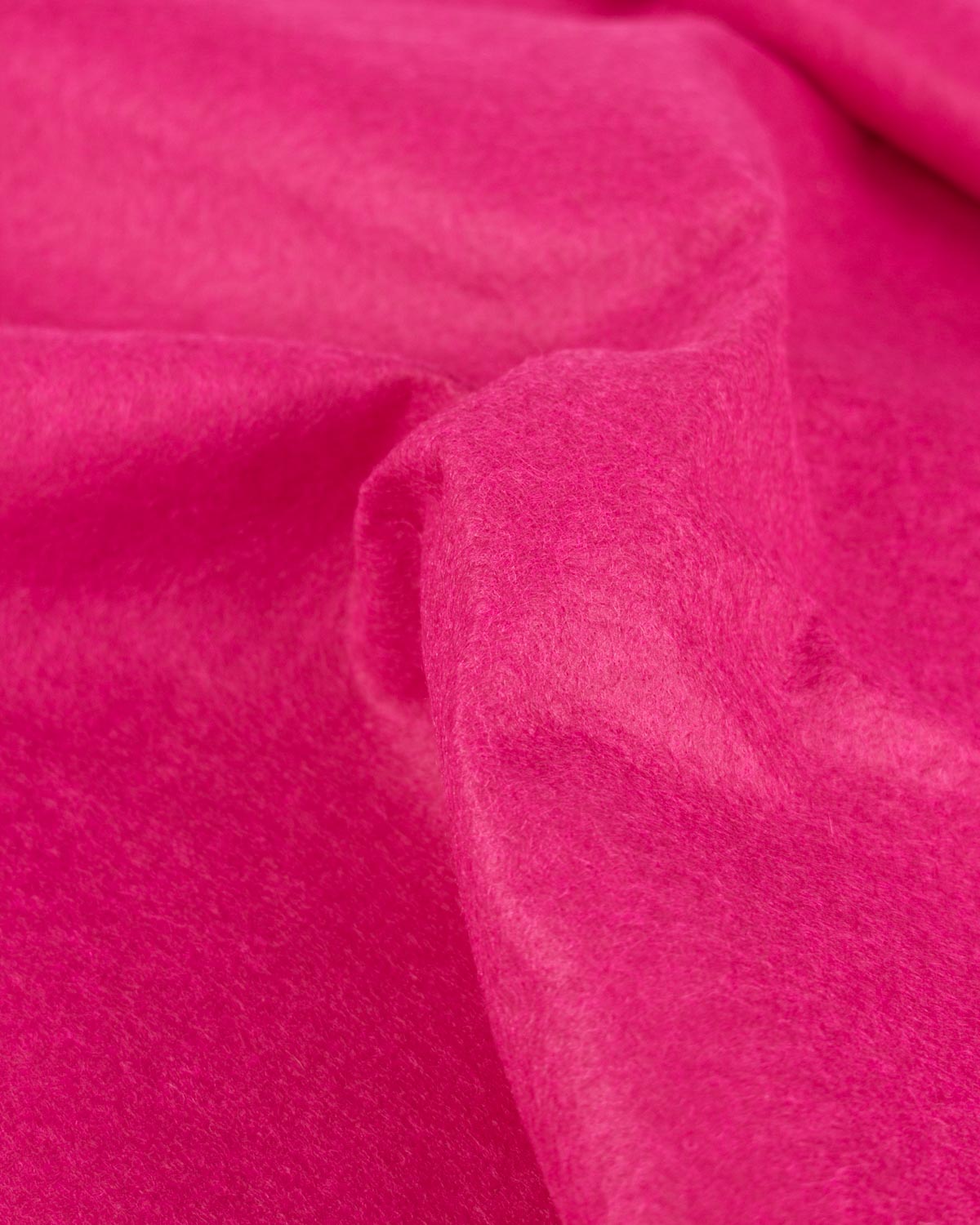 A close up of bright pink draped wool and viscose felt fabric, gathered to show its firm structure and texture. 